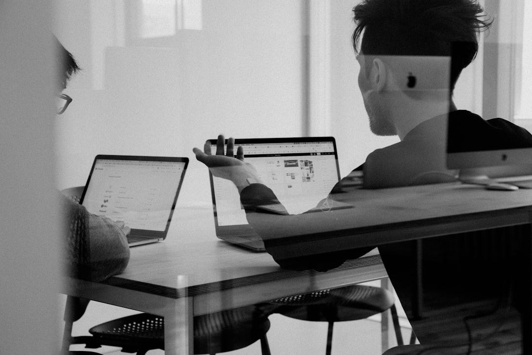 A black and white photo of two people working at a desk.